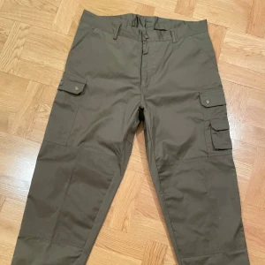 Jakt/fritidsbyxa - Oanvända fritidsbyxor EuroHunt, stl D100. Ofodrade. Snedfickor fram, fickor m dragkedjor bak, enkel resp dubbel benficka på vardea benet. Justerbart benslut. Vindtäta och vattenavvisande. Fintvätt 40 grader. Nypris ca 900:-