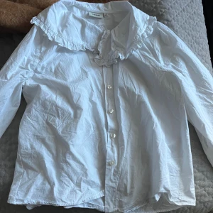 Vit blus från Dobber - Säljer en superfin vit blus från Dobber i storlek M. Den har en söt volangkrage och knappar framtill. Perfekt för både vardag och fest! 💫
