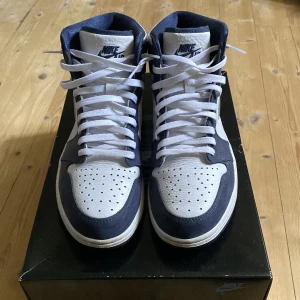 Air Jordan 1 Japan Midnight Navy Metallic silver - Säljer ett par snygga Nike Air Jordans i blått och vitt. Skorna har klassisk snörning och är i mycket bra skick. Perfekta för både vardag och fest! De har en stilren design med det ikoniska Air Jordan-märket på sidan.