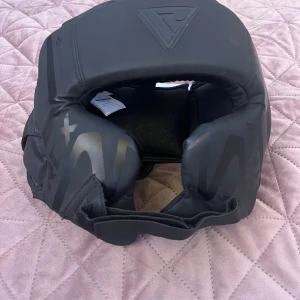 Svart huvudskydd från RDX för kampsport - Säljer splitterny svart huvudskydd från RDX med prislappen kvar. Aldrig använd och säljer pga att jag behövde sluta på muay thai. Perfekt för kampsportsträning med bra passform och skydd. Tillverkat i slitstarkt material med justerbar rem för optimal komfort. Märket RDX är känt för sin kvalitet och hållbarhet. Nypris 650 (även väldigt dyr frakt måste jag påpeka…)