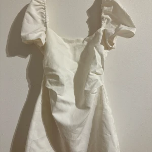 Vit klänning från Zara - Säljer en superfin vit klänning från Zara med puffiga kortärmar och en snygg öppen rygg med snörning. Perfekt för sommarens fester eller en mysig midsommar. Klänningen har en elegant och luftig design som passar både till vardags och festligare tillfällen.