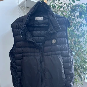 Svart dunväst från Stone Island - Säljer en snygg svart dunväst från Stone Island. Västen har en dragkedja framtill och är perfekt för höst och vår. Den är i mycket bra skick och har en normal passning.