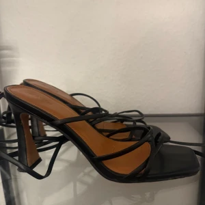 Svarta klackskor med snörning - Snygga svarta klackskor med skön klack och elegant snörning. Perfekta för en utekväll eller fest. De har en stilren design med öppen tå och smala remmar som ger en chic look. Passar bra till både klänning och byxor.