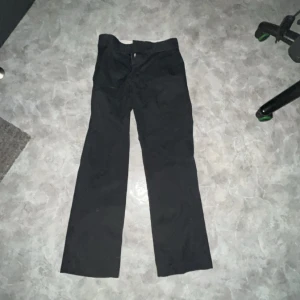 Dickies byxor svarta - Säljer ett par svarta byxor i storlek 28x30. De är tillverkade av 65% polyester och 35% bomull, vilket gör dem både slitstarka och bekväma. Perfekta för vardagsbruk eller mer formella tillfällen. Byxorna har en klassisk stil och passar bra till olika outfits.