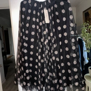 Svart prickig kjol - Säljer en superfin svart kjol med stora vita prickar. Den är i ett luftigt och lätt material, perfekt för både fest och vardag. Klänningen har en lös passform och är i nytt skick med etikett kvar. Perfekt för att göra ett statement på nästa fest!