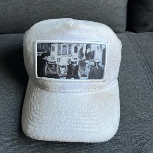 Vit keps med tryck.Emiliopendenza - Säljer en unik vit keps med ett coolt svartvitt tryck på framsidan. Kepsen har en mjuk och fluffig yta som ger den en annorlunda look. Perfekt för att sticka ut i mängden! Passar bra till både vardag och fest.