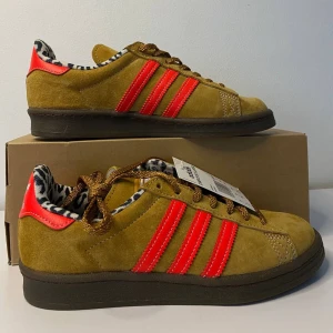 Adidas Campus 80 X Large - Snygga Adidas Campus 80 X Large i mocka med coola röda detaljer och leopardmönstrat foder. Skorna har en klassisk design med snörning och kommer med extra skosnören i olika färger. Perfekta för att ge din outfit en unik touch!