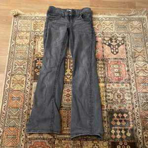 Säljer ett par grå bootcut jeans från Gina Tricot i storlek 158. De har en klassisk femficksdesign och stängs med dragkedja och knapp. Perfekta för en avslappnad stil och passar bra till både vardag och fest. Skicket är bra och de är bekväma att bära.