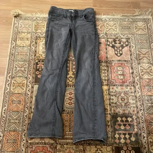 Grå bootcut, lågmidjade jeans från Gina Tricot - Säljer ett par grå bootcut jeans från Gina Tricot i storlek 158. De har en klassisk femficksdesign och stängs med dragkedja och knapp. Perfekta för en avslappnad stil och passar bra till både vardag och fest. Skicket är bra och de är bekväma att bära.