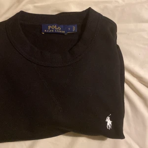 Svart tröja från Polo Ralph Lauren - Säljer en klassisk svart tröja från Polo Ralph Lauren i storlek S. Tröjan är i nytt skick med etikett kvar och har en broderad vit logga på bröstet. Perfekt för både vardag och fest. Pris kan diskuteras
