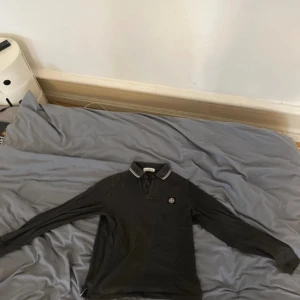 Grå pikétröja från Stone Island - Säljer en snygg svart pikétröja från Stone Island i slim fit. Tröjan har en klassisk krage med vita ränder och en broderad logga på bröstet. Size M slimfit