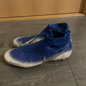 Blå Nike phanton - Säljer ett par blå Nike Phantom fotbollsskor i bra skick. De har en cool design med vit och blå färgkombination och är perfekta för fotbollsträning eller match. Skorna har en tight passform och är gjorda i syntetmaterial för bästa prestanda på planen. Dessa helt näsan helt nya använt få gånger 