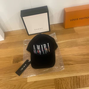 Svart keps från Amiri - Snygg svart keps från Amiri med justerbar passform. Den har ett coolt broderat märke framtill och mesh-detaljer baktill för extra ventilation. Perfekt för en avslappnad stil eller att lyfta din outfit. Kepsen är i nytt skick och kommer med originaltaggar.