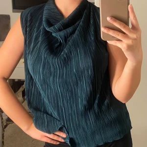 Mörkgrön plisserad topp från Anna Field - Snygg mörkgrön plisserad topp från Anna Field. Den är ärmlös och har en elegant draperad krage. Perfekt för både vardag och festliga tillfällen. Materialet är mjukt och ger en lyxig känsla. Passar bra till både jeans och kjol! PERFEKT TILL NYÅR❤️ storlek står ej men har för mig att de va S eller XS