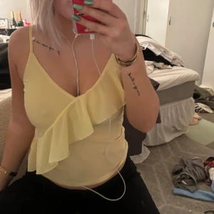 Gul volangtopp - Säljer en söt gul topp med volangdetaljer. Den är ärmlös och har en v-ringad design som ger en somrig känsla. Perfekt för varma dagar eller en avslappnad fest. Toppen är i bra skick och passar perfekt till jeans eller kjol.