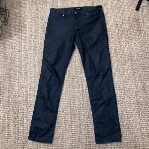 J.Lindeberg waxed denim - Snygga svarta byxor från J.Lindeberg i bra skick. De har en klassisk design med knappar och dragkedja framtill. Perfekta för både vardag och fest. Passar till alla säsonger och är ett måste i garderoben!