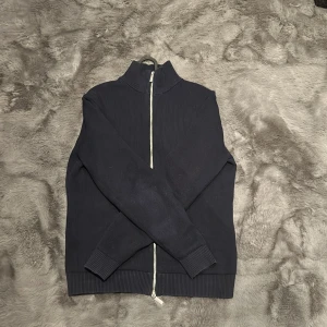 Mörkblå Fullzip - Säljer en stilren mörkblå fullzip från selected homme. Perfekt för kyliga dagar, den har långa ärmar och en hög krage för extra värme. Materialet känns mjukt och bekvämt, och den ribbade nederkanten ger en snygg passform. Passar både till vardags och lite finare tillfällen.Sällan och sparsamt använd då jag märkte att den va för liten nästan direkt. 