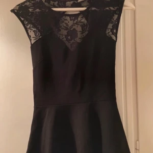 Svart tröja  med spetsdetaljer - Elegant svart tröja  med vackra spetsdetaljer vid halsen och axlarna. Perfekt för festliga tillfällen. Klänningen har en figurnära passform och är ärmlös, vilket ger en stilren look.