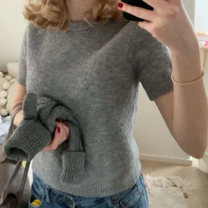 Grå stickad tröja - Säljer en supermysig grå stickad tröja i bra skick. Den har korta ärmar och en klassisk rund halsringning. Perfekt för både vår och höst när det är lite kyligt ute. Passar till både jeans och kjol för en avslappnad look.