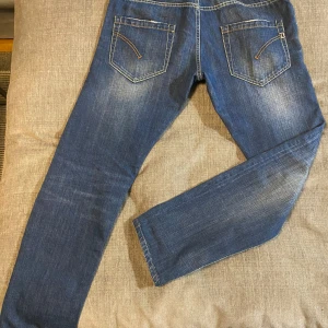 Blå jeans med slitningar - Säljer ett par snygga blå jeans från Dondup med coola slitningar och kontrastsömmar. De har en klassisk femficksdesign och en bekväm passform. Perfekta för vardagsbruk eller en avslappnad utekväll. Passar bra till sneakers eller kängor. Storlek 36 skulle säga att det passar dig best som har 34/32