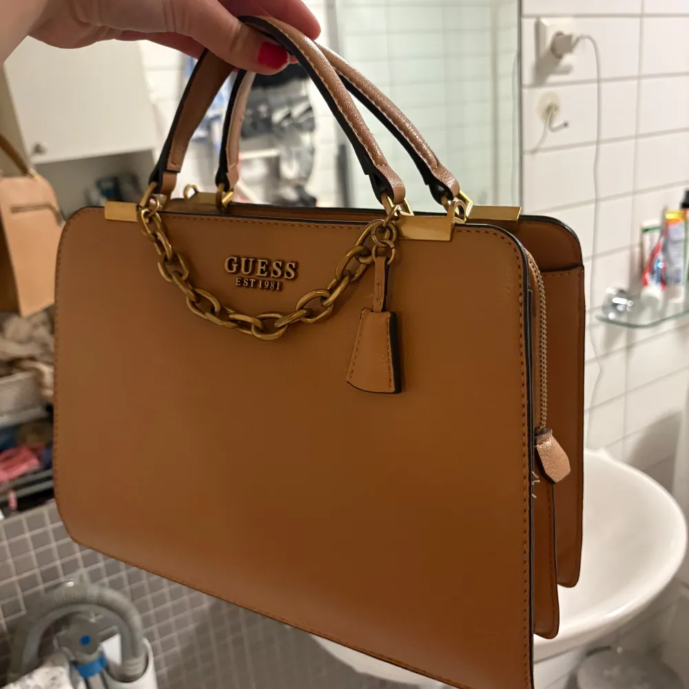 Snygg brun handväska från Guess i mycket bra skick. Väskan har en elegant kedjedetalj och dragkedja för säker förvaring. Perfekt för både vardag och festliga tillfällen. Stilren design som passar till det mesta!. Laukut & Käsilaukut.