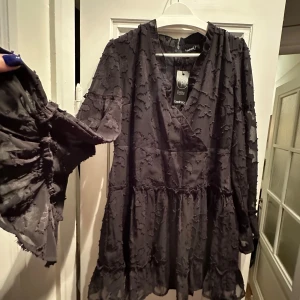 Svart klänning med volangdetaljer - Snygg svart klänning från Boohoo i nytt skick (prislapp). Den har ett vackert mönster och volangdetaljer som ger en romantisk touch. 
