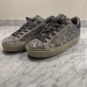 Glittriga sneakers från Golden Goose - Säljer ett par snygga glittriga sneakers med lite högre sula från Golden Goose. De är använda ett fåtal gånger men ser nästan helt sprillans nya ut. De är silverglittriga med grå mocha detaljer. Skorna är i jätte bra skick och skorna är riktigt bekväma. Hör av dig vid intresse samt frågor! Pris är ej hugget i sten!😉🤩🤩