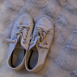 Vita sneakers från Gant - Säljer ett par vita sneakers från Gant i bra skick. Lite skitiga. De har klassisk snörning och en stilren design med Gant-loggan på sidan. Perfekta för vår och sommar, dessa sneakers är både bekväma och snygga. Passar till de flesta outfits!😍