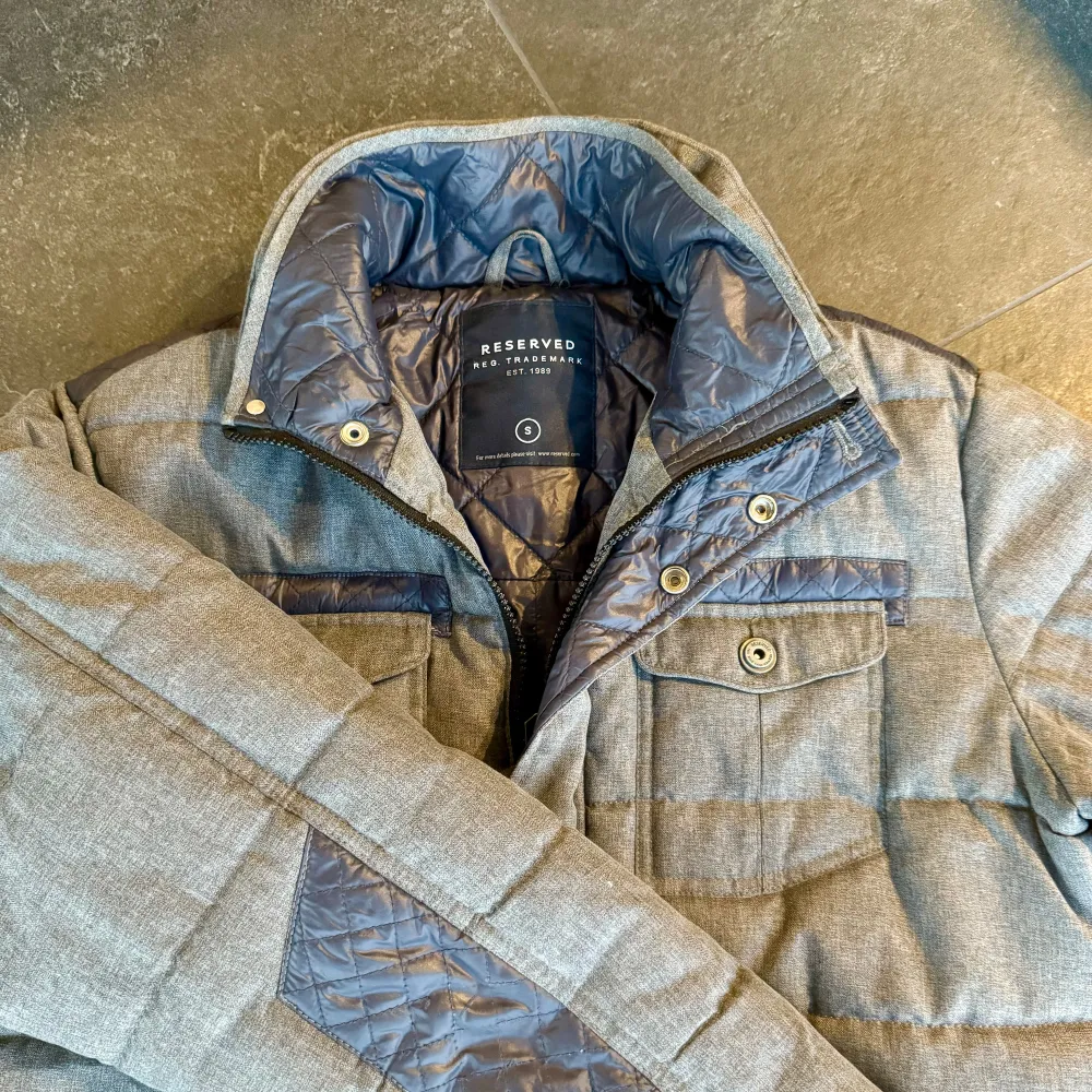Säljer en snygg grå quiltad jacka från Reserved. Den har en stilren design med dragkedja och knappar framtill. Jackan har flera praktiska fickor och en hög krage för extra värme. Perfekt för höst och vinter! 🧥. Takit.
