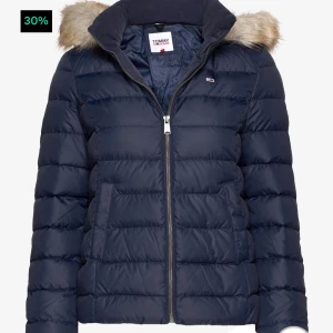 Mörkblå dunjacka från Tommy Hilfiger - Säljer en snygg och varm mörkblå dunjacka från Tommy Hilfiger. Jackan har en avtagbar huva med fuskpäls och dragkedja framtill. Den är helfodrad och gjord av 100% återvunnen polyester. Perfekt för kalla dagar! Säljer på grund av att den är lite för tajt för mig, men väldigt fin! Helt ny