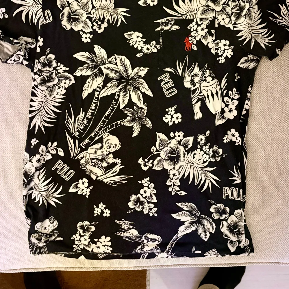 Säljer en snygg svart t-shirt från Ralph Lauren med ett coolt blommönster i vitt. Den har en liten röd logga på bröstet och är i custom slim fit. Perfekt för sommaren eller en avslappnad dag ute. 🌺. T-shirts.