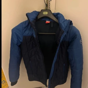 Blå pufferjacka från Puma - Säljer en snygg blå pufferjacka från Puma i storlek 152. Jackan har en dragkedja framtill och är perfekt för kyliga dagar. Den är i mycket bra skick och har en sportig stil som passar både till vardags och träning. Perfekt för höst och vinter!