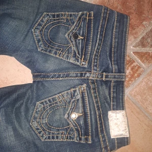 True religion jeans - Säljer ett par snygga mörkblå jeans med coola detaljer på bakfickorna, ena fickan saknar dock en knapp. De har en tight passform och är perfekta för både vardag och fest. Modellen är tight men man kan själv sy de bootcut om man vill. 💖