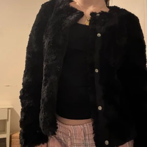 Svart pälsjacka - Säljer en supermjuk och fluffig svart pälsjacka. Den har en klassisk design med knappar framtill och är perfekt för att hålla sig varm och stilren under kyliga dagar. Jackan är i mycket bra skick och passar perfekt för höst och vinter. Perfekt för att ge din outfit en lyxig touch!