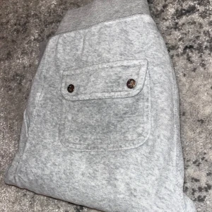 Gråa Juicy Couture byxor - Säljer ett par grå Juicy Couture byxor i bra skick. De har en bekväm resårmidja med snörning och praktiska fickor med knappar bak. Supermjuka och sköna! Uppsydda cirka 7cm i benet, lite kortare än original längden för storleken. 