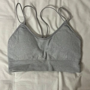 Grå ribbad linnetopp - Säljer en snygg grå ribbad linnetopp med smala axelband. Perfekt för sommardagar eller som ett lager under en tröja. Toppen är i mycket bra skick och har en enkel men stilren design.