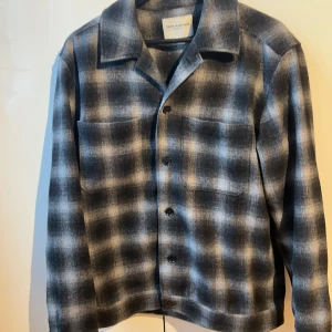 Rutig overshirt från These Glory Days - Säljer en snygg rutig overshirt från These Glory Days i storlek XL. Den har en klassisk krage och knappar framtill. Färgerna går i blått, grått och svart, perfekt för höst och vår. Två stora bröstfickor ger en cool look. Passar både till vardags och lite mer uppklädda tillfällen.
