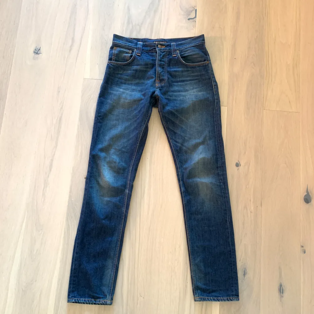 Säljer ett par mörkblå jeans i bra skick. De har en snygg slitningseffekt på framsidan och baksidan, vilket ger dem en cool look. Jeansen har en klassisk femficksdesign och knappar i midjan. Perfekta för både vardag och fest!. Jeans & Byxor.