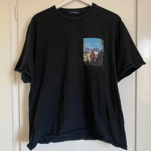 Svart t-shirt från Johnundercover - Säljer en svart t-shirt från Johnundercover i storlek L. Den har en cool tryckdetalj på bröstet. T-shirten är gjord av 100% bomull med vissa delar i polyester. Perfekt för en avslappnad stil!