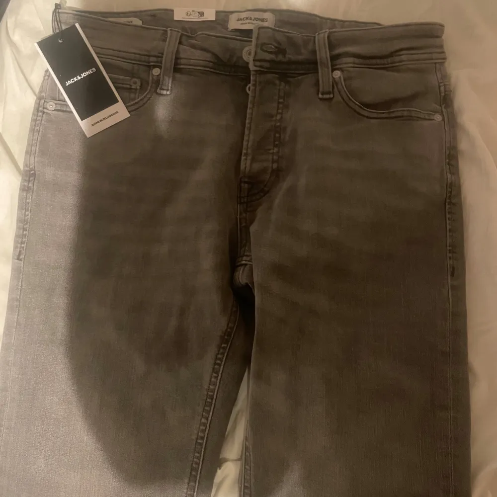 Säljer ett par snygga grå jeans från Jack & Jones i nytt skick. De har en tapered passform och är midwaist. Byxorna har knappar istället för dragkedja och är perfekta för både vardag och fest. De är gjorda i ett bekvämt denim-material.. Jeans & Byxor.