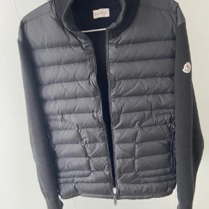 Moncler cardigan  - Säljer en snygg svart jacka från Moncler i mycket bra skick. Jackan har en fin design med dragkedja framtill och långa ärmar. Och den är både stilren och bekväm. Passar perfekt för en casual look eller en dag ute på stan. 