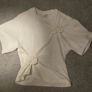 Vit t-shirt med blom detaljer💕🌸 - Säljer en söt vit t-shirt med två blommor framtill. Sjukt snygg till fest eller bara vanlig vardag🥹(lånad bild, skriv för egna)