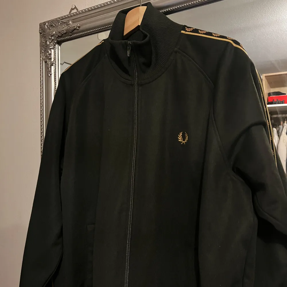 Säljer en snygg svart jacka från Fred Perry i mycket bra skick. Den har en dragkedja framtill och coola detaljer med Fred Perry-loggan längs ärmarna. Perfekt för höst och vår, och den har en normal passform. Jackan är långärmad och gjord i ett bekvämt material.. Jackor.