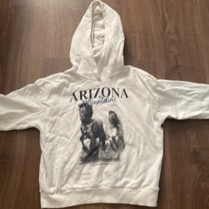 Vit hoodie från KappAhl med Arizona-tryck - Säljer en vit hoodie från KappAhl i storlek 146/152. Den har ett coolt tryck med texten 'Arizona Mountains' och en bild av hästar. Perfekt för en avslappnad stil och passar bra till både jeans och mjukisbyxor. Hoodien är i bra skick och redo för nya äventyr! 🐴