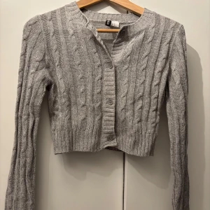 Grå stickad kofta från Divided - Säljer en superfin grå stickad kofta från Divided i storlek XS. Den har ett snyggt flätmönster och knappar framtill. Perfekt för höst och vinter när du vill hålla dig varm och stilren. Passar både till vardags och lite finare tillfällen. 🧶✨