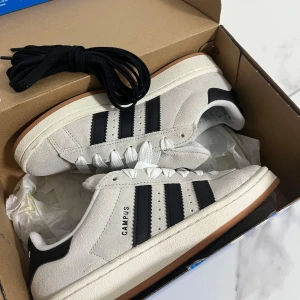 Adidas Campus sneakers i beige och svart - Säljer ett par snygga Adidas Campus sneakers i beige mocka med svarta detaljer. Perfekta för vardagen. Skorna är i nytt skick och kommer med extra skosnören. Storlek på de är 38 2/3 men skulle säga att de passar upp till 39 också.              (Använda endast en gång). Priset kan diskuteras! 