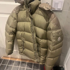 Olivgrön pufferjacka från Moncler - Säljer nu min unika olivgröna pufferjacka från Moncler. Retail pris: 12 800kr. Jackan är perfekt för kalla dagar med sin tjocka vaddering och har en praktisk huva. Den har en dragkedja framtill och Monclers logga på ärmen. Perfekt för vintern och hösten! Priset kan diskuteras vid snabbaffär! 