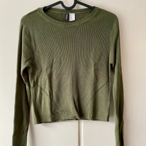 Olivgrön ribbad tröja från H&M - Säljer en olivgrön ribbad tröja från H&M i storlek M. Tröjan har en croppad passform och långa ärmar. Den är i bra skick och supermjuk, idealisk för en casual look. Passar både till jeans och kjol!