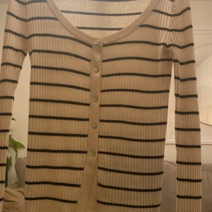 Beige och svart randig kofta - Säljer en superfin beige kofta från Zara med svarta ränder. Den är ribbad och har knappar framtill. Perfekt för höst och vår, och funkar både till vardags och fest. Långärmad och i bra skick!