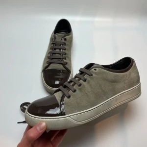 Lanvin skor  - Säljer ett par snygga Lanvin sneakers i beige mocka med bruna lackdetaljer på tån och hälen. Skorna har en klassisk snörning och en bekväm vit sula. Perfekta för både vardag och fest! Uk6 passar 41. Hör av dig vid frågor 